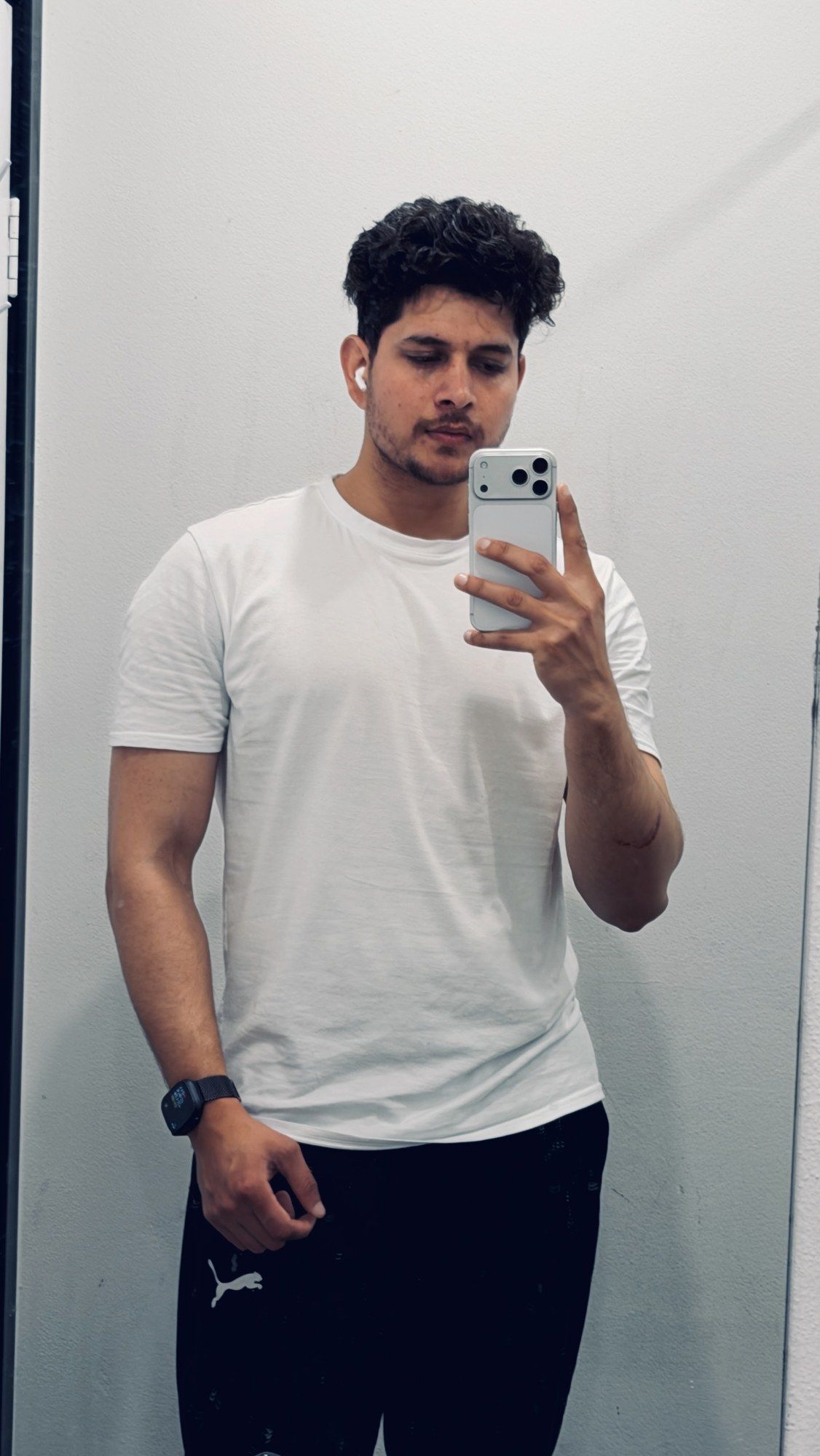 Mirror selfie at the gym in a white T-shirt.