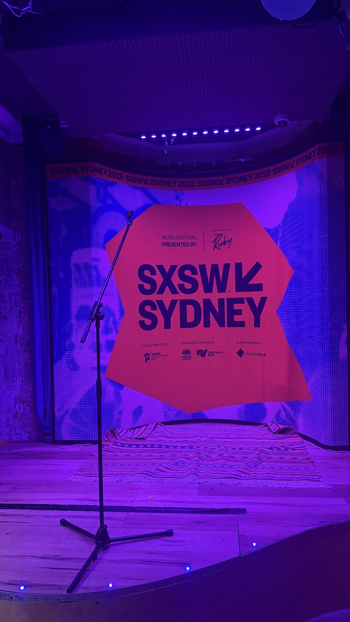 A pink SXSW Sydney banner on an empty purple-lit stage.