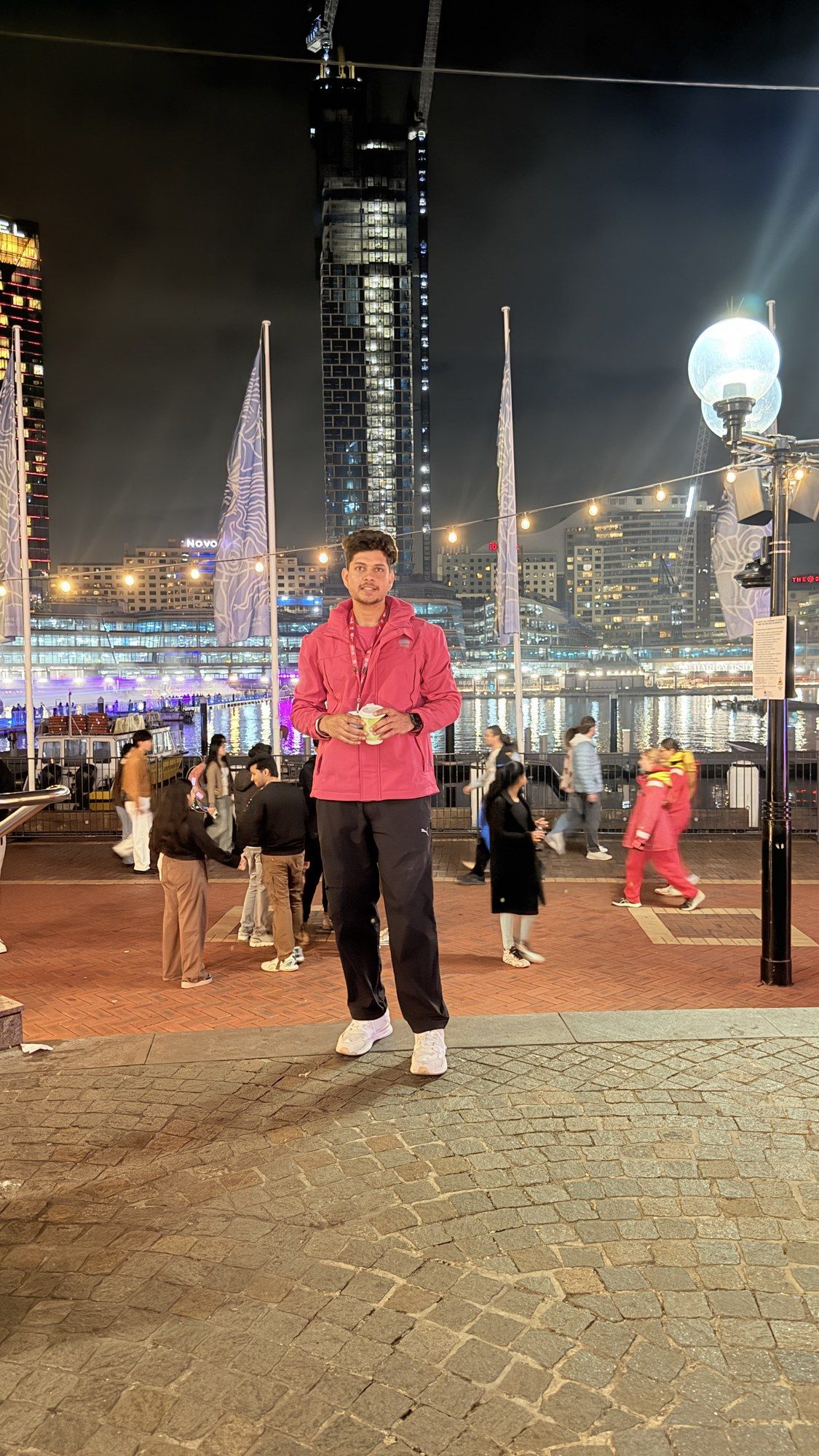 Manish in a pink volunteer jacket on the Vivid promenade at night.